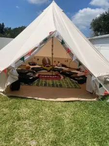 A canvas tent decorated with festive flags for a birthday, featuring a football-themed interior with a rug resembling a football field and plush football-shaped pillows.