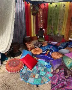 A colorful bohemian-style tent interior featuring an array of vibrant cushions, rugs, and draped fabrics, perfect for the ultimate adult party.