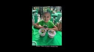 Young girl in green shirt at a table, smiling and holding two bowls of colorful slime, with text "Thank You | slime time | jojo's shake bar" displayed.