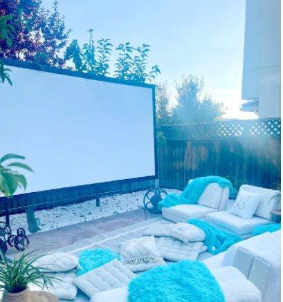 A backyard transformed into an outdoor movie theater, complete with a movie screen, cozy couches, and a bell tent for a party atmosphere.