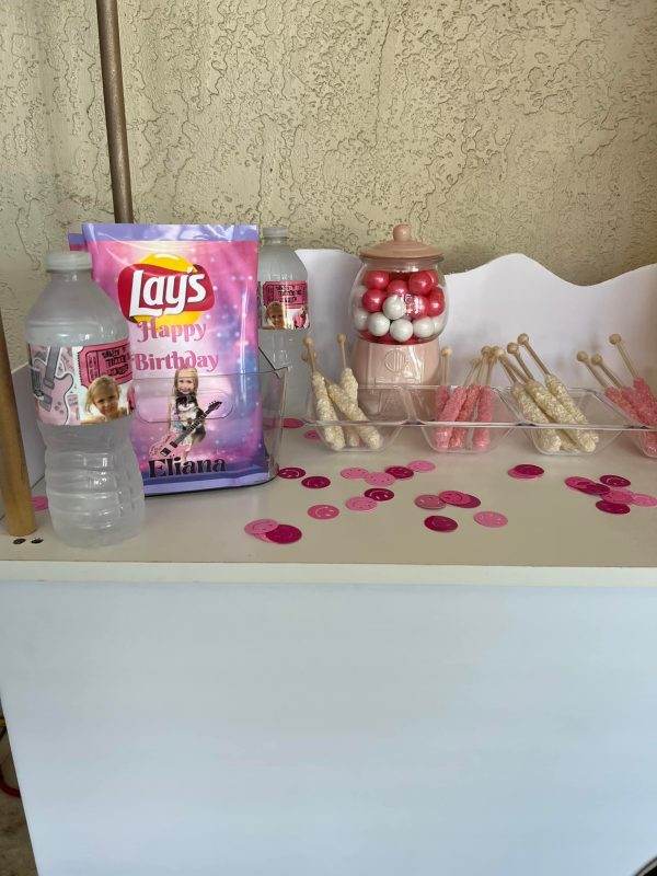 A pink and white party table adorned with snacks and a bottle of water, creating a Large Greenery Photo Backdrop with Neon Sign atmosphere.