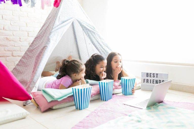 Three girls sitting in a Lakeland teepee with popcorn and a laptop.