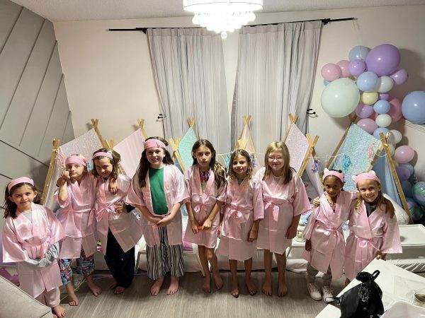 Kids lined up wearing cute spa robes in a modern living room with teepee rentals and balloons.