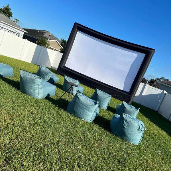 Outdoor inflatable projector screen with outdoor seating sitting in front of it on the grass.