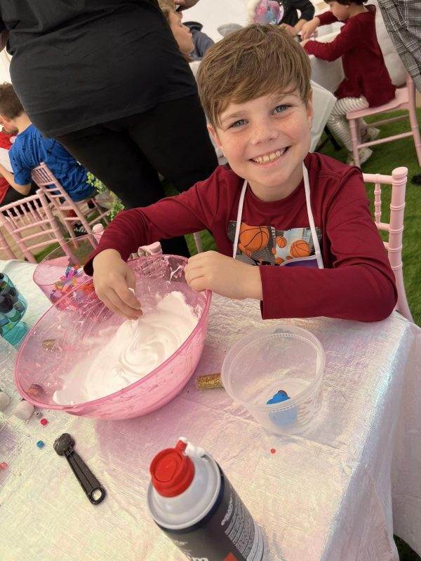 A young boy smiling at a table with a bowl of icing during a party.