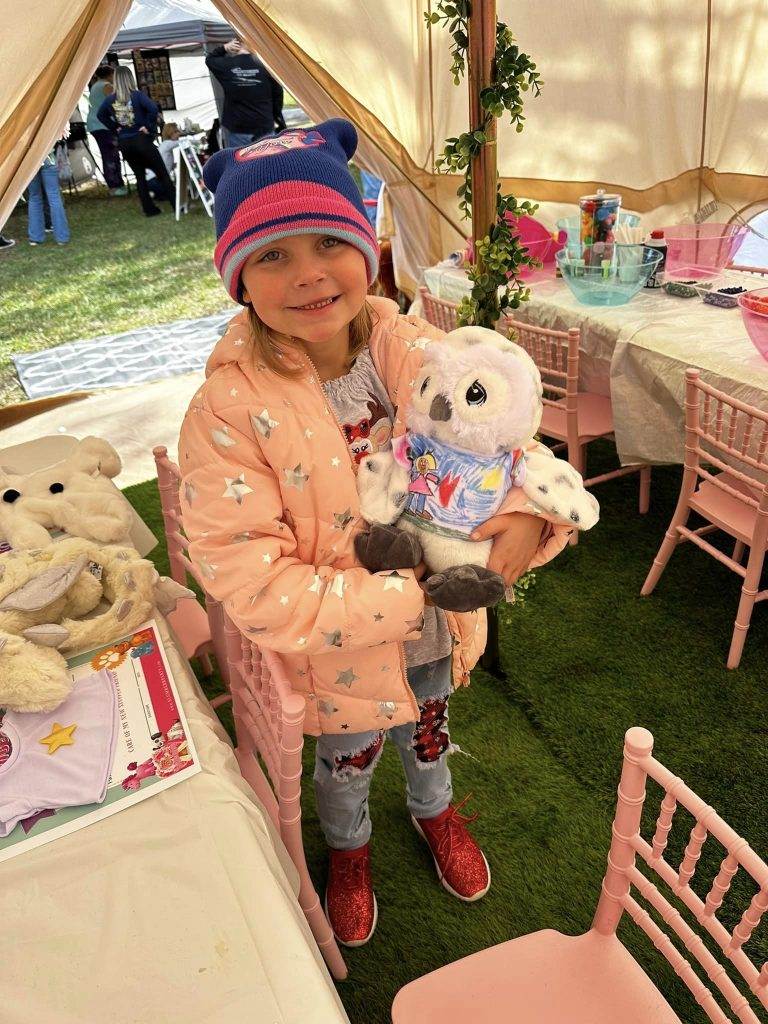 A girl holding a teddy bear in a teepee tent.