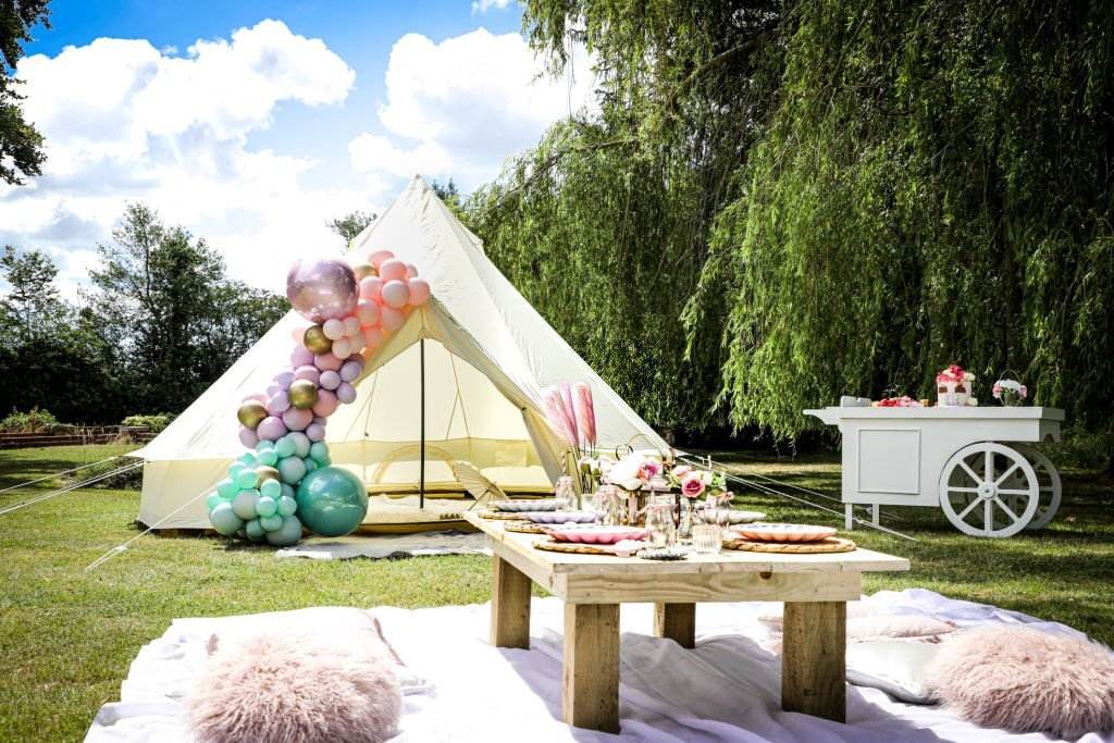 A decorated teepee and a table with party supplies are set up outdoors on grass, with pillows and a white canopy, showcasing an exceptional party rental service.