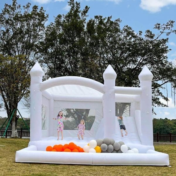 Children playing in a 15FT X 13FT White Bounce House with colorful balls on a grassy field under a cloudy sky.