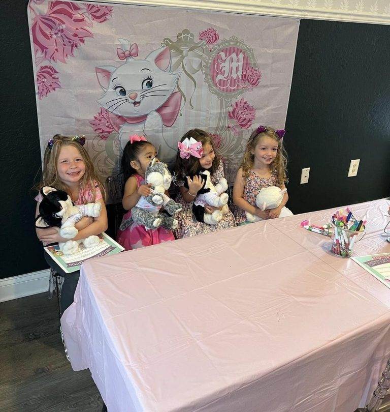 A group of girls sitting at a table with stuffed animals, enjoying a glamping experience.