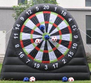 Inflatable dartboard with velcro soccer balls stuck on various numbers, located on a grass field in front of a building, perfect for birthday party add-ons.