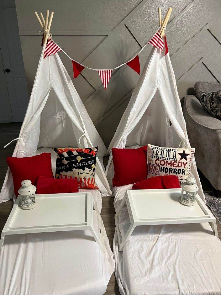 Two white teepee beds with red and white decorations for a glamping party.