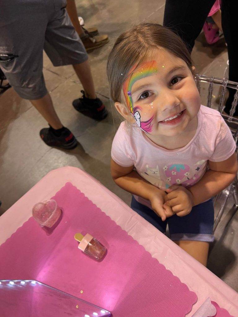 A little girl sitting at a pink table with makeup on her face in Lakeland.