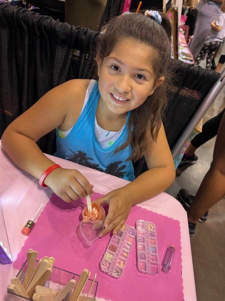 A young girl smiling at a table at a convention, surrounded by colorful slime.