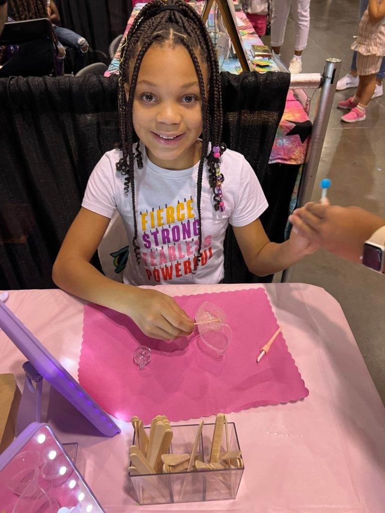 A young girl smiling at a table with a pink tablecloth while enjoying glamping.
