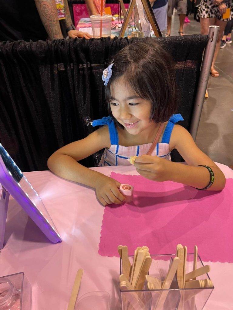 A little girl sitting at a table with a pink mirror, enjoying a slime party.