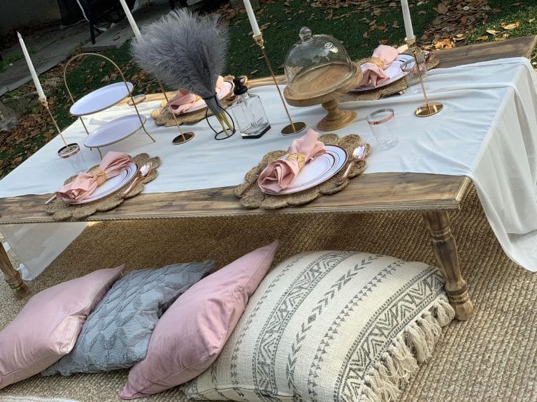 A glamping party table set up with pink pillows and candles.