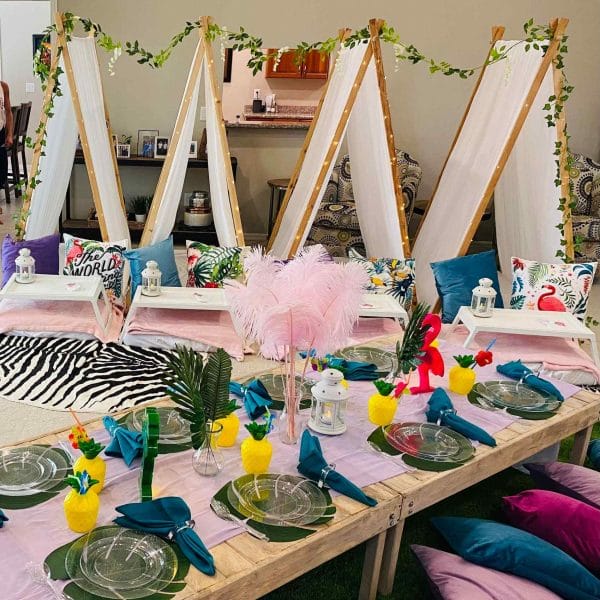 Art-themed sleepover party setup with easels, paintbrushes, colorful table settings, and decorative elements in a bright room.