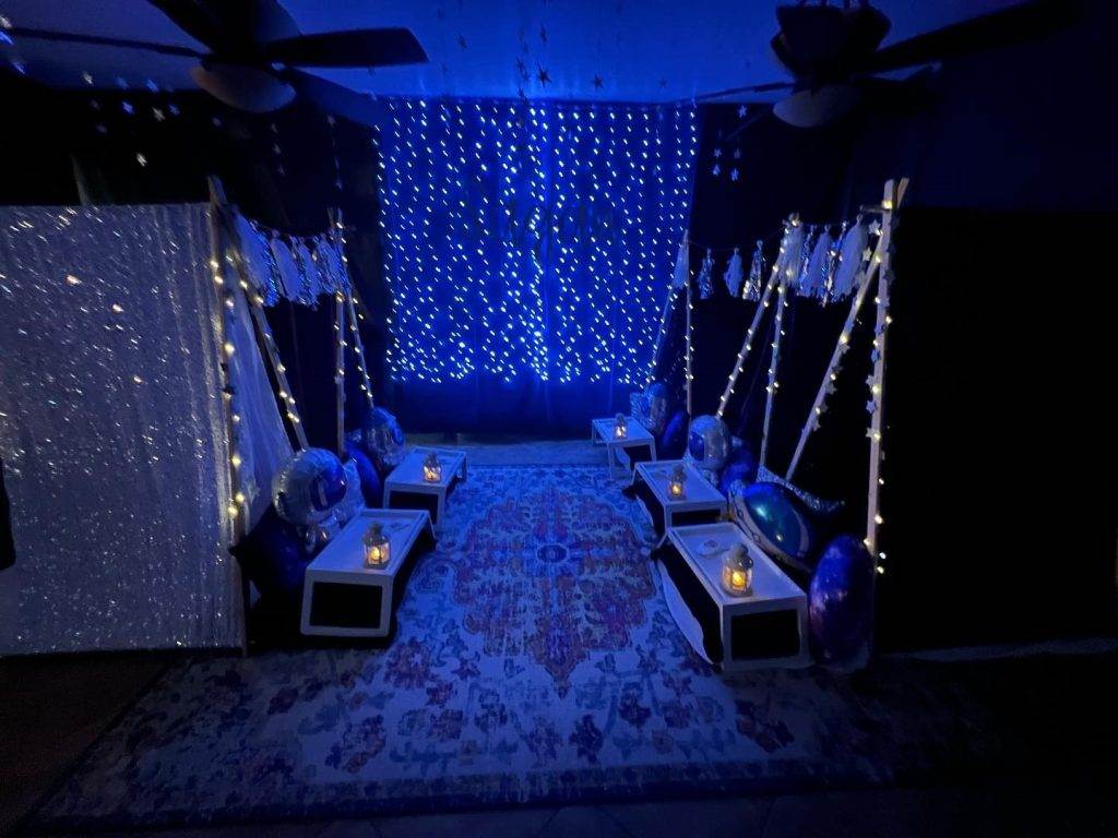 A party room decorated with blue lights, a rug, and a teepee.