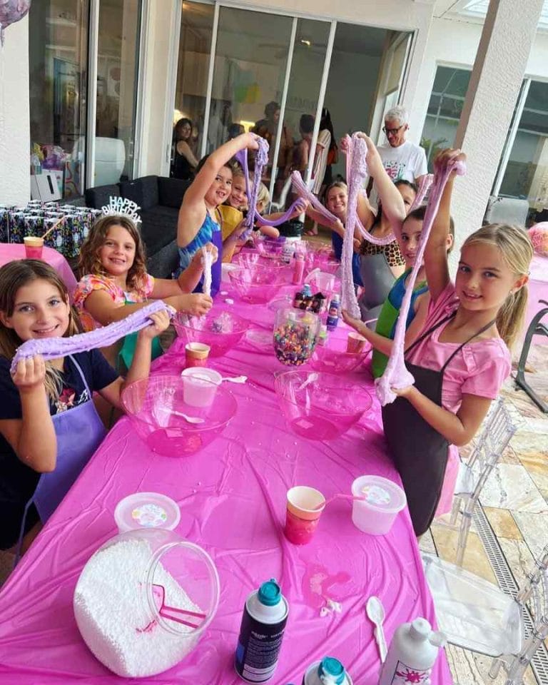 A group of girls at a pink table with balloons and slime.