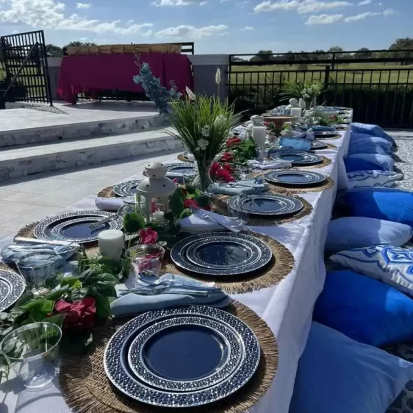 Outdoor dining table set for a meal with elegant blue and white plates, woven placemats, floral centerpieces, and a scenic Central Florida backdrop.