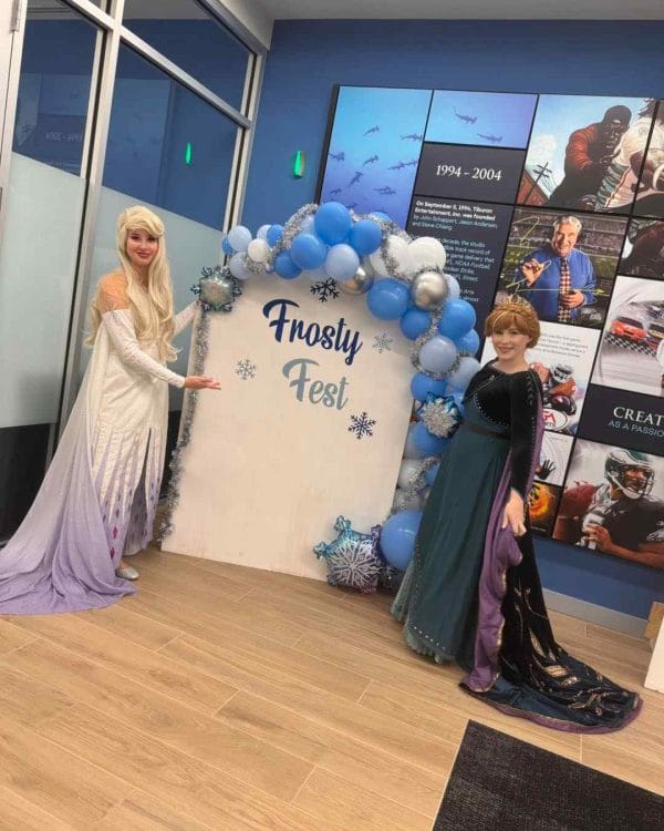 Two frozen princesses standing in front of a Party sign