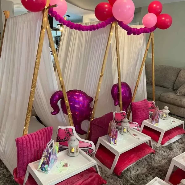 Indoor party setup with a Barbie theme, featuring small pink couches, tables, a balloon arch, and a draped tent for kids parties.