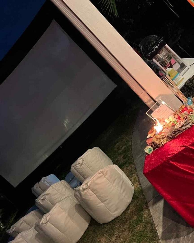 A party scene featuring an outdoor movie screen adorned with comfortable red bean bags.