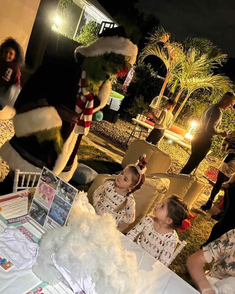 A group of children are sitting at a table with a Santa Claus mascot at a party.