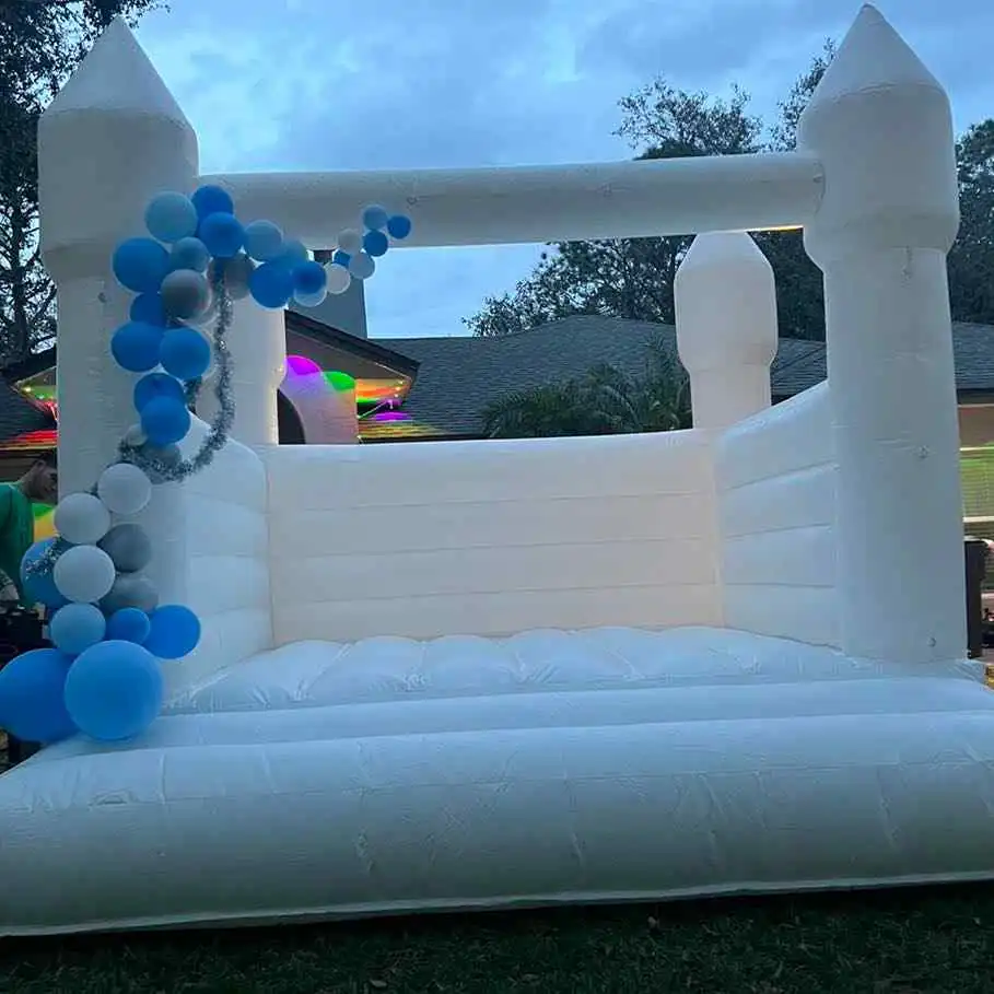 Inflatable white castle with blue and white balloons in an outdoor setting at dusk.