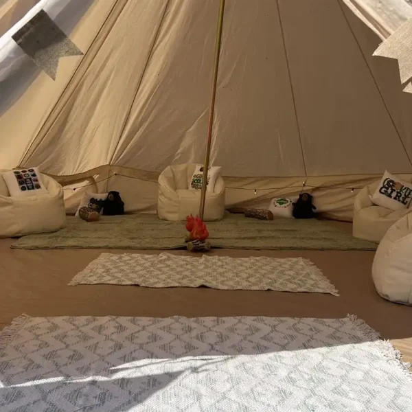 A cozy glamping tent with white beanbag chairs arranged around a small central fire pit, various cushions, and rugs on the ground. The tent is well-lit, creating a warm and inviting atmosphere perfect for a Harry Potter Themed Party.