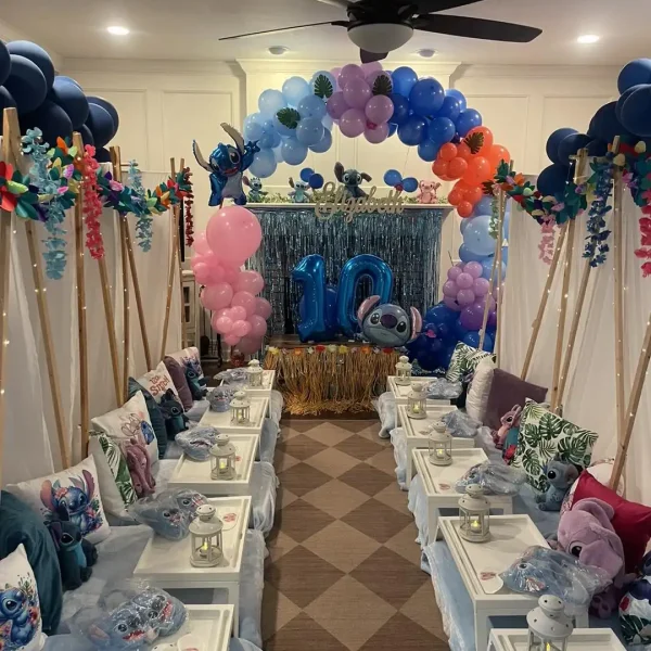 A decorated indoor space for a 10th birthday celebration with a blue and pink balloon arch, Harry Potter Themed Party decorations, and tables set up with plates, pillows, and small lanterns.
