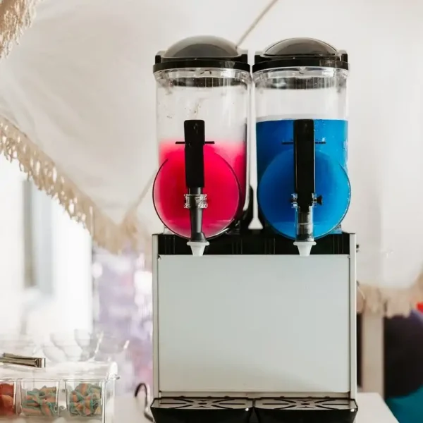 Our Event Photography Packages now feature a dual beverage dispenser, with a pink drink in the left chamber and a blue drink in the right chamber. Additionally, small containers filled with individually wrapped items on the left make it an ideal complement to our offerings.