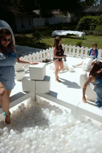Adults and children enjoy playing in a white ball pit outdoors, enclosed by a small white fence, making it an ideal setting for capturing memories with our Event Photography Packages.