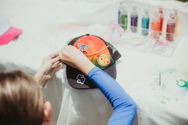 A person with a blue sleeve is placing embroidered patches on a black and red cap on a white table, capturing the moment as part of Event Photography Packages.