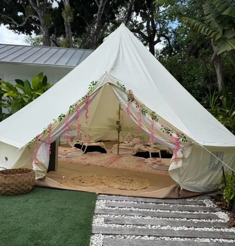 A large white canvas tent with floral garlands at the entrance, set up with low tables and rugs inside, stands on a lawn with a stone path—perfect for events from a premier party shop in Central Florida.
