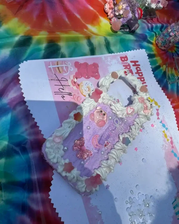 Decorate your Extra Large Teepee Rental party setup with a pastel pink and purple phone case featuring cream-like frosting, beads, and gummy bear charms, displayed on tie-dye cloth and birthday-themed paper for added flair.
