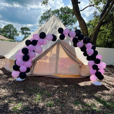 A bell tent rented out for a birthday party lined up with purple and black balloons
