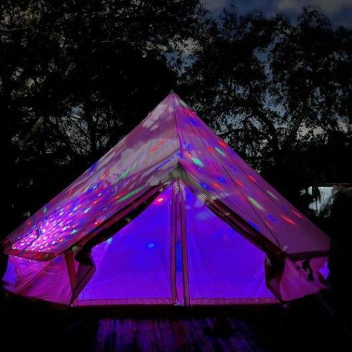 A Bell Tent lit up at night with purple lights, creating a magical and vibrant party atmosphere for glamping enthusiasts.